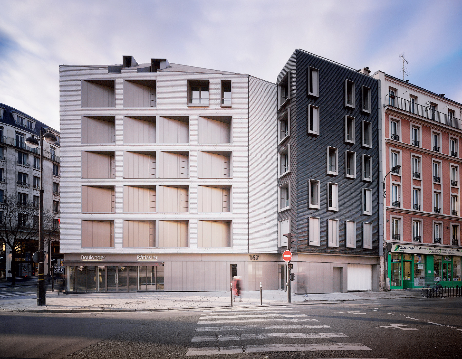 Z ulice pôsobí dom ako trblietavá hra tehál rôznych odtieňov, ktorá však rešpektuje svoje okolie a spoluvytvára genius loci námestia.