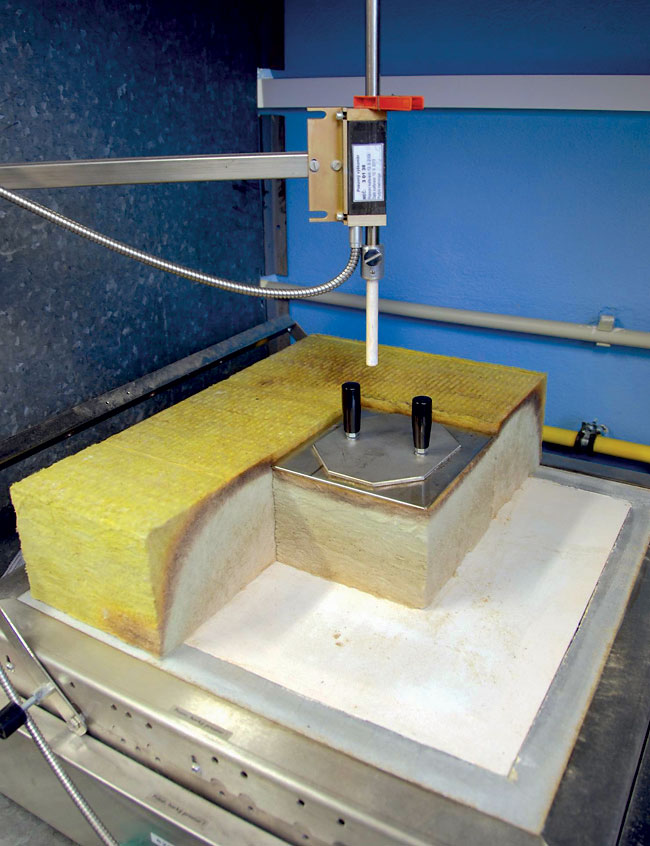 Obr. 4 Pohľad na meracie zariadenie pri najvyššej prevádzkovej teplote. Na obrázku je zrejmé vypálenie spojiva pri izolácii z minerálnej vlny (sivá oblasť) po takmer celej výške vzorky pri pôsobení teploty 700 °C počas 3 dní